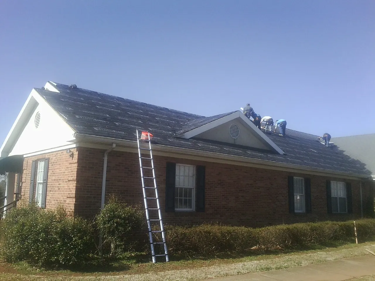 Crew tearing shingles off a brick ranch roof with a ladder set — Emergency Roof Repair work by our crew in Lathrop
