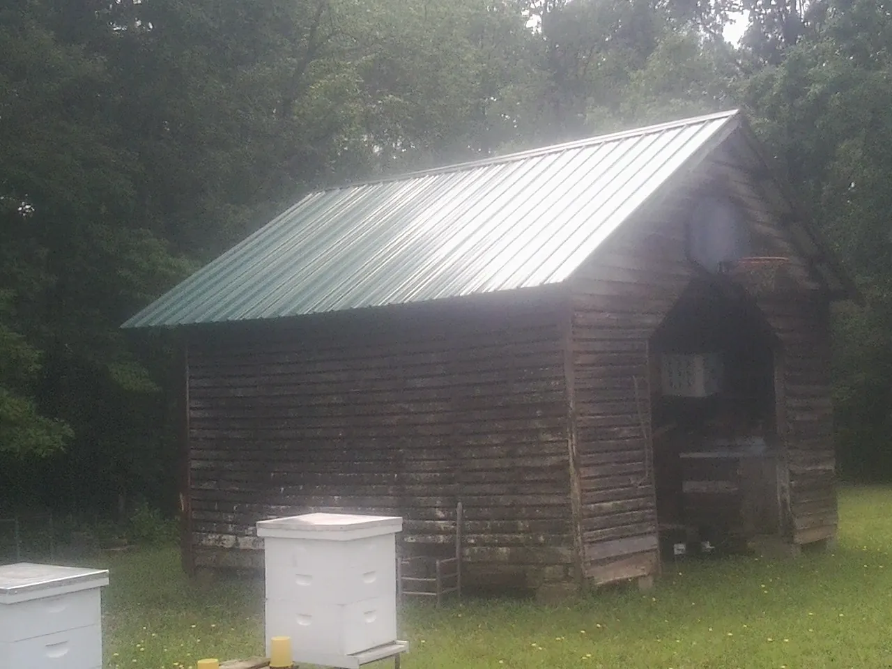 Green metal roof on a weathered barn beside stacked beehives in Lathrop