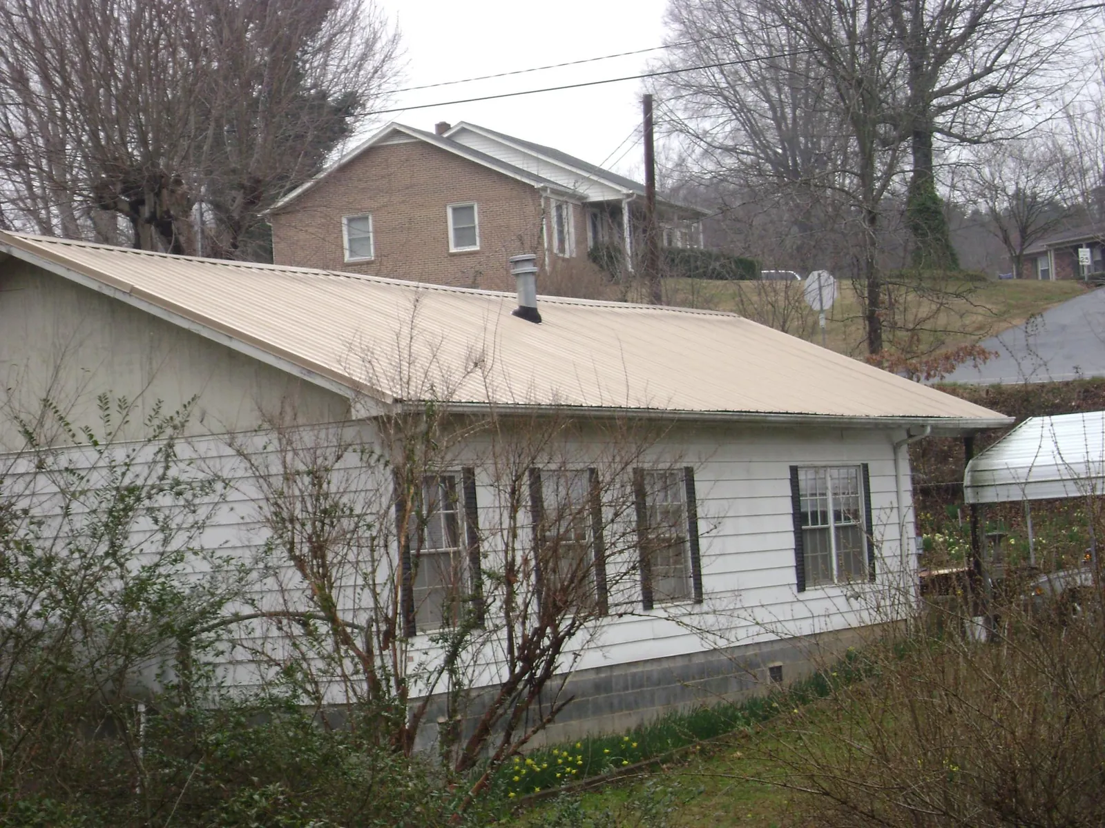 Tan metal roof on a white sided house set into a hillside — Commercial Roofing by Roofing Brothers in Lathrop